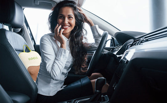 A woman sits in a car with a portable AVOHUG massage pillow on the seat
