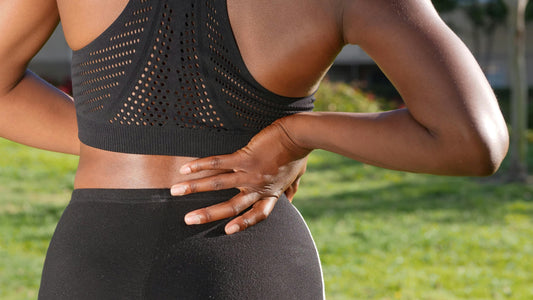 A woman is shown from the back, with her right hand resting on her lower back.