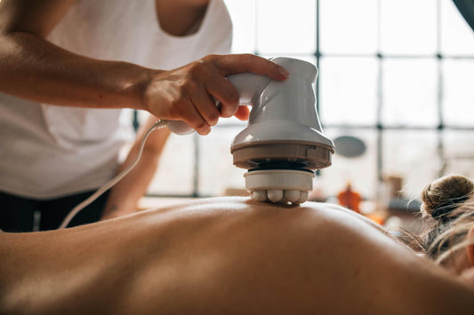 A person lying face down on a massage table while a massage therapist uses a massage device to work on their back, providing a relaxing and therapeutic experience.
